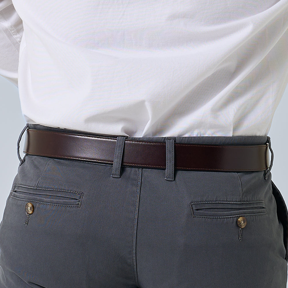 Person wearing a white shirt, gray pants, and a brown belt against a light background