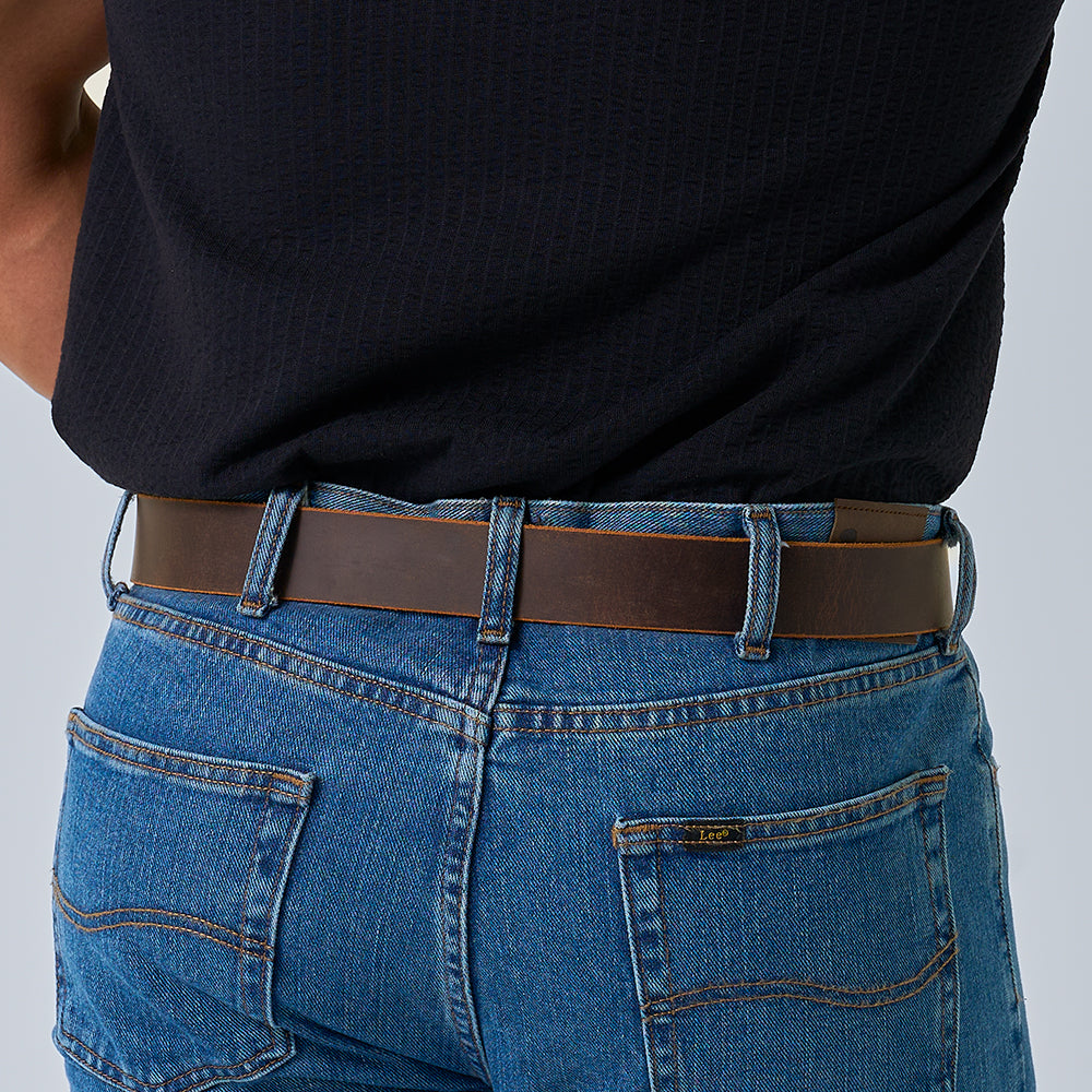 A person wears The Crazy Horse by Hanks Belts—a retro leather belt—over blue jeans and a black shirt. Photo from the back emphasizes the waistband, belt, and loops.