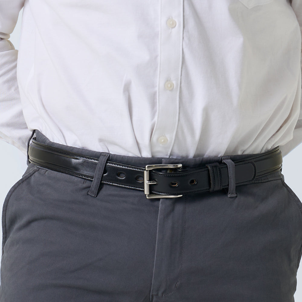 A person wearing a white button-up shirt tucked into gray pants, secured with The Esquire Raised premium leather belt by Hanks Belts.