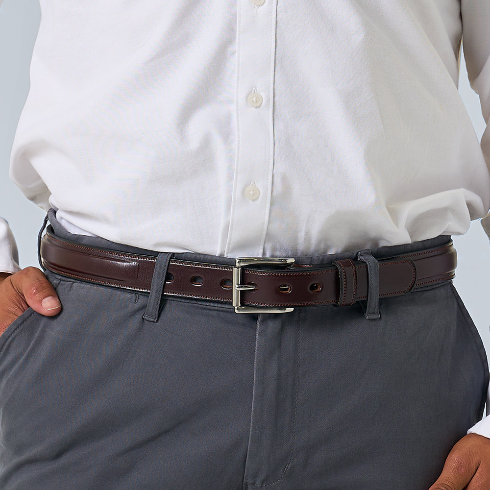 A person wearing gray pants with a white button-up shirt tucked in, sporting The Esquire Raised belt by Hanks Belts in dark brown, hands resting on their hips.