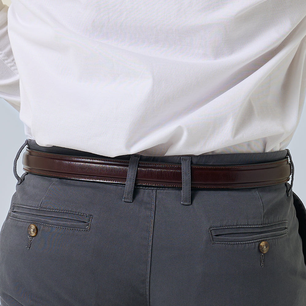 A person wears a white shirt tucked into gray pants with buttoned back pockets, accessorized by Hanks Belts' The Esquire Raised dress belt in dark brown English Bridle leather. Image focuses on the waist and lower back.