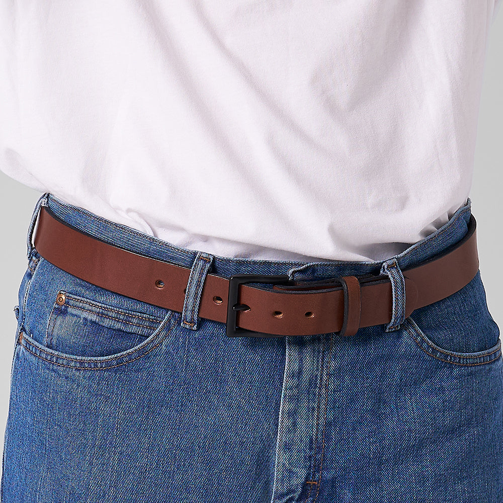A person wears blue jeans with front pockets and visible stitching, paired with a white shirt and The Everyday full-grain leather belt from Hanks Belts around their waist.