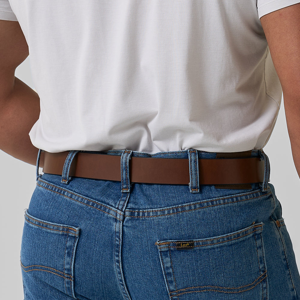 A person shown from the back wears a white t-shirt tucked into blue jeans with Hanks Belts’ The Double Prong Everyday retro belt; the brand label appears above the right back jean pocket.