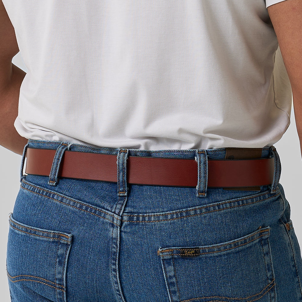 A person is shown from the back wearing blue jeans and a Hanks Belts "The Gunner" belt with a tucked-in white shirt. The image focuses on the waist and hip, highlighting this sturdy CCW belt from Hanks Belts.