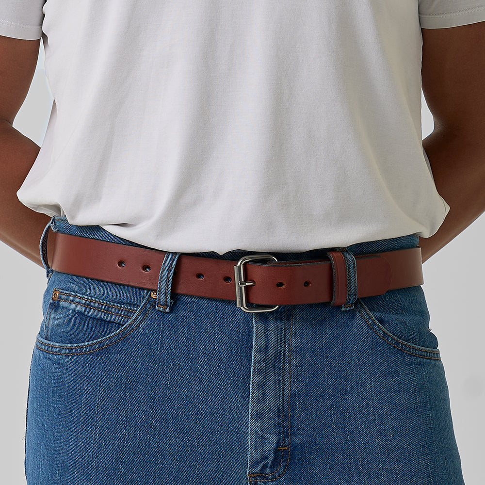 A person wearing a white t-shirt, blue jeans, and The Gunner belt by Hanks Belts with a silver buckle, shown from the waist down against a neutral background.