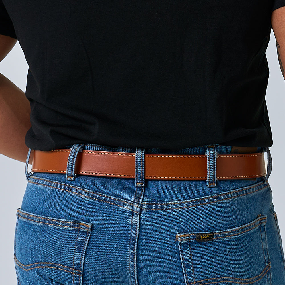 A person wearing blue jeans and a black shirt is shown from the waist down and back, with The Gunner Stitched full-grain leather CCW belt by Hanks Belts, featuring visible stitching, threaded through the belt loops.