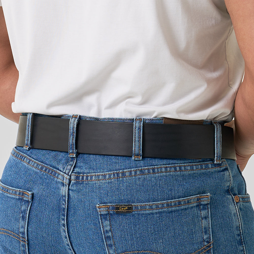 A person wearing blue jeans and a white t-shirt showcases The Marshall gun belt by Hanks Belts, with the sturdy black belt—2" wide—threaded through the jean loops in a waist and lower back focused image.