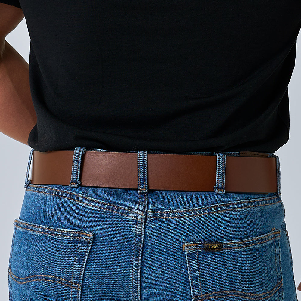 A person wears The Marshall by Hanks Belts—a sturdy leather garrison belt—with a black shirt tucked into blue jeans. The image highlights the belt and jean details at the back waist.