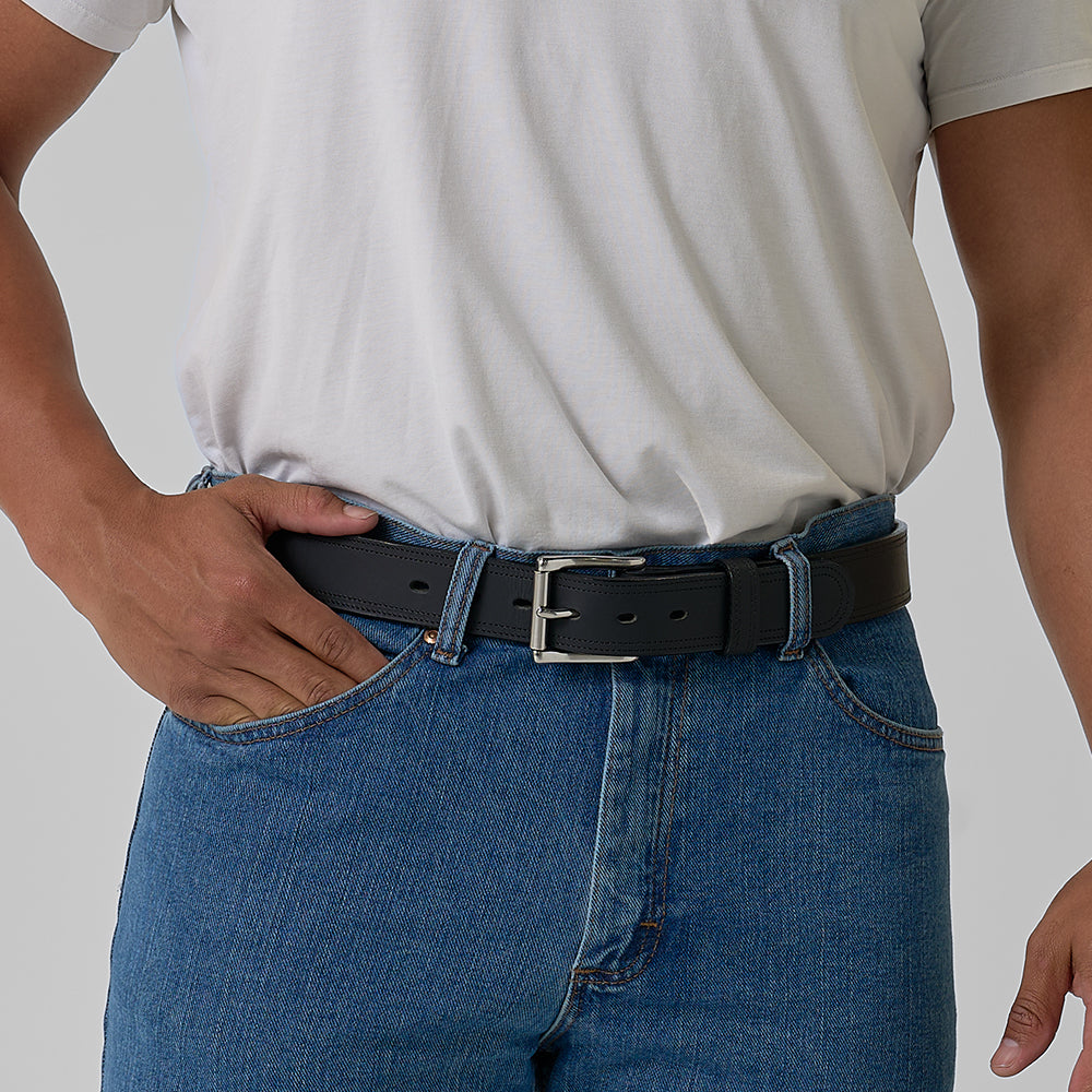 Person wearing a black belt with a silver buckle, white shirt, and blue jeans on a gray background