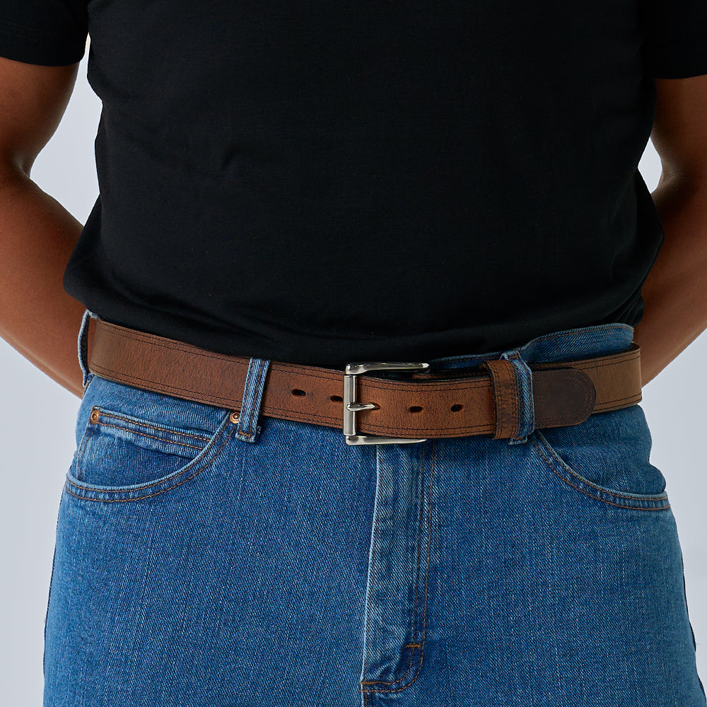Person wearing a brown belt with a black shirt and blue jeans on a light gray background