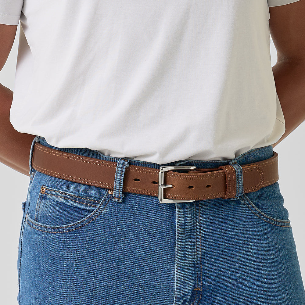 Person wearing a brown belt with blue jeans on a plain background