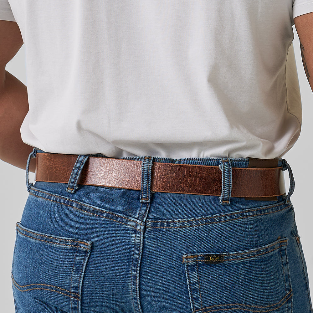 A person wearing blue jeans with visible belt loops and back pockets, accessorized with The Rustic Glazed belt by Hanks Belts, shown from the back and waist down.