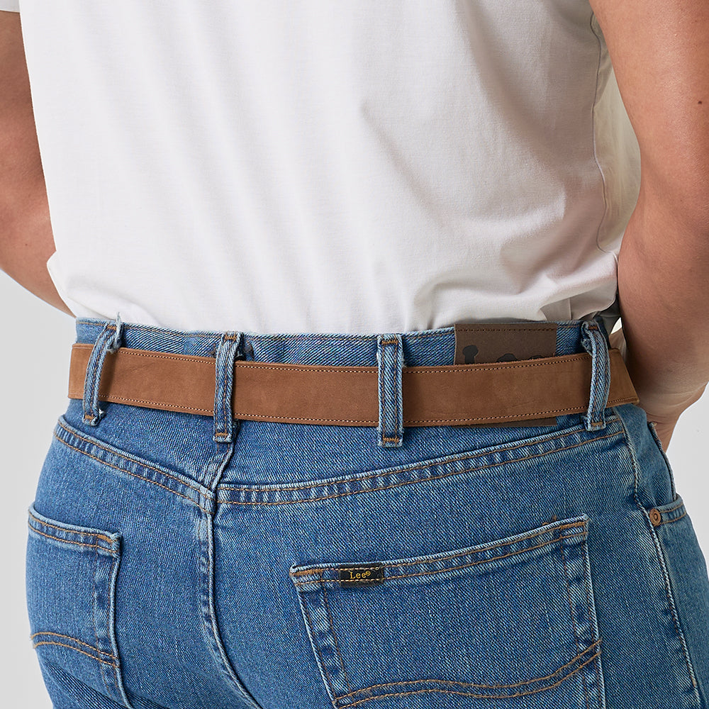 A person shown from the back wears blue jeans with visible stitching and pockets, a white shirt, and The Suede - 1.25" brown leather belt by Hanks Belts.