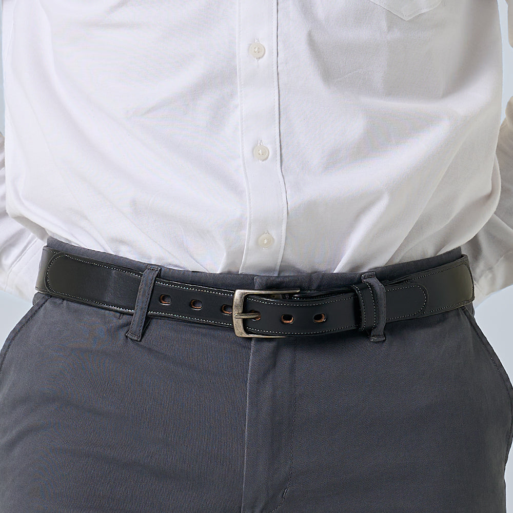 A person wearing a white button-down shirt tucked into gray pants, styled with The Teton Tapered belt by Hanks Belts—crafted from vegetable tanned leather and finished with a sleek silver buckle.