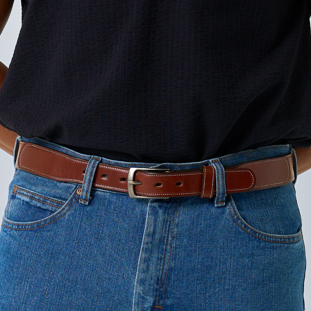 A person shown from the waist down wears blue jeans with The Teton Tapered belt by Hanks Belts, crafted from handcrafted leather, paired with a tucked-in dark textured shirt.