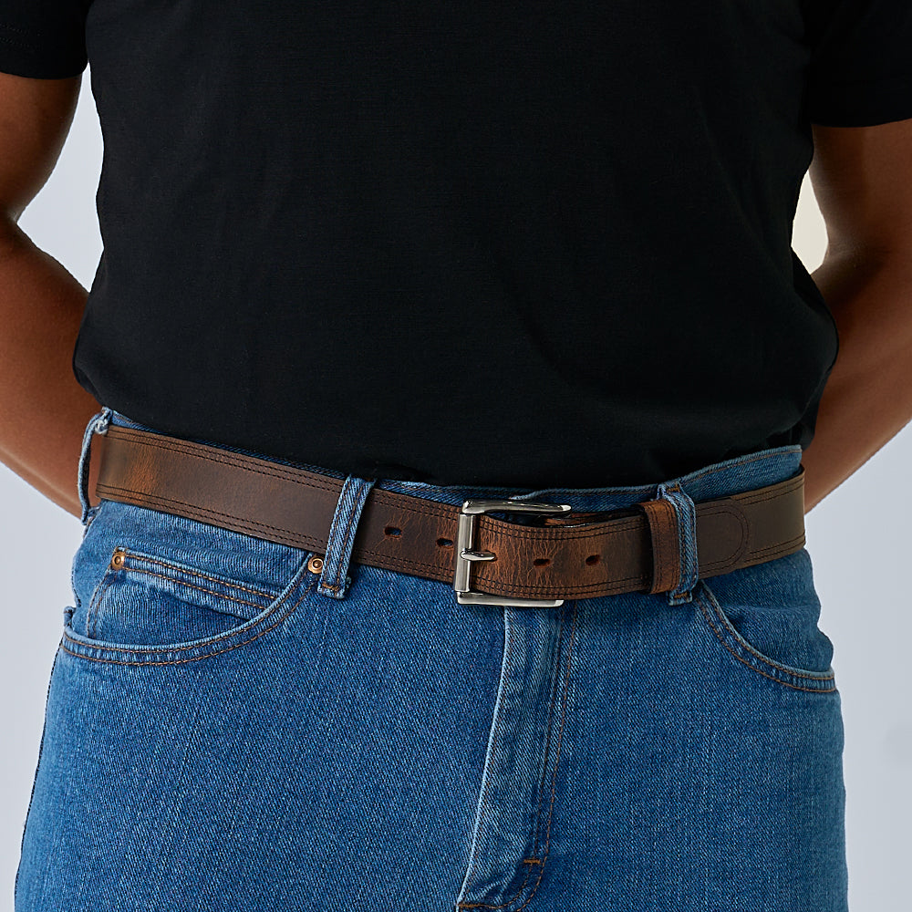A person wearing a black t-shirt, blue jeans, and The Wyoming Bison belt by Hanks Belts with a silver buckle stands with hands behind their back.
