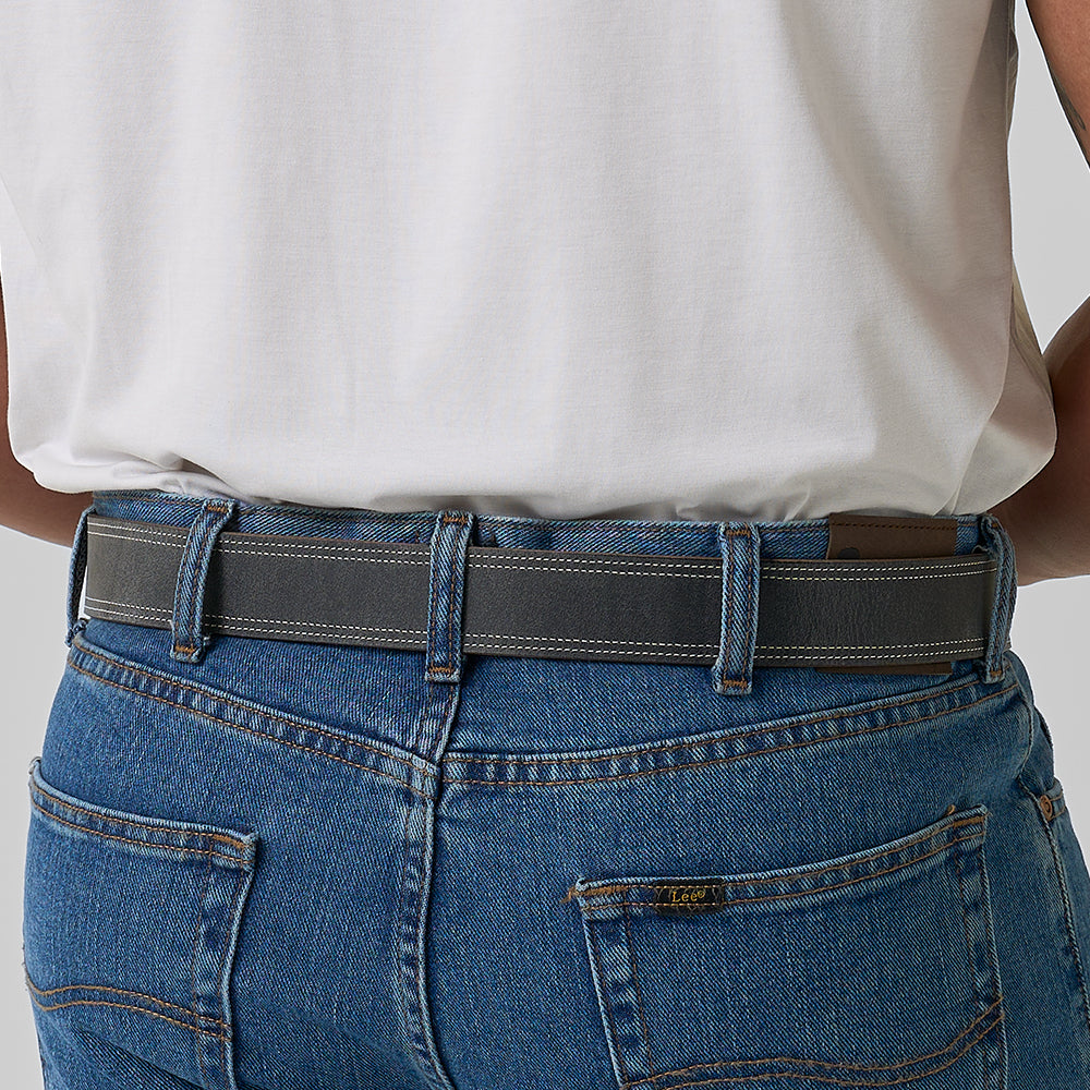 A person seen from behind, wearing blue jeans and a white shirt, has The Wyoming Bison belt by Hanks Belts in dark gray threaded through their belt loops. The image highlights the waist and lower back area.