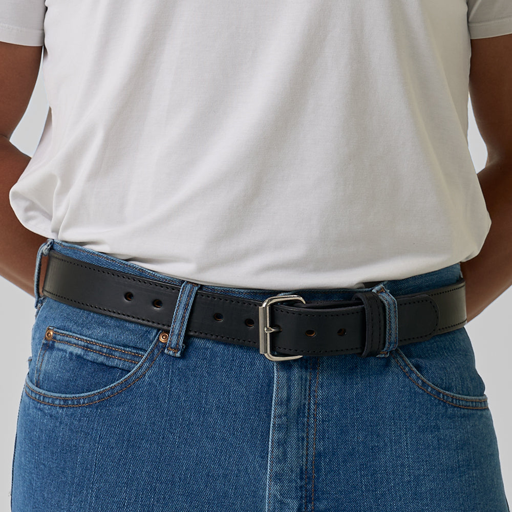 A person wears a plain white t-shirt with blue jeans, accessorized with Hanks Belts' The Xtreme - 1.5", a black heavy duty belt featuring a silver buckle.