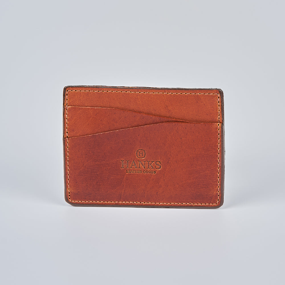 The Cumberland Bison Card Holder by Hanks Belts features brown bison leather, visible stitching, and "Hanks Leather Goods" embossed on the front, shown on a light gray background. This USA-made wallet is crafted for durability and timeless style.