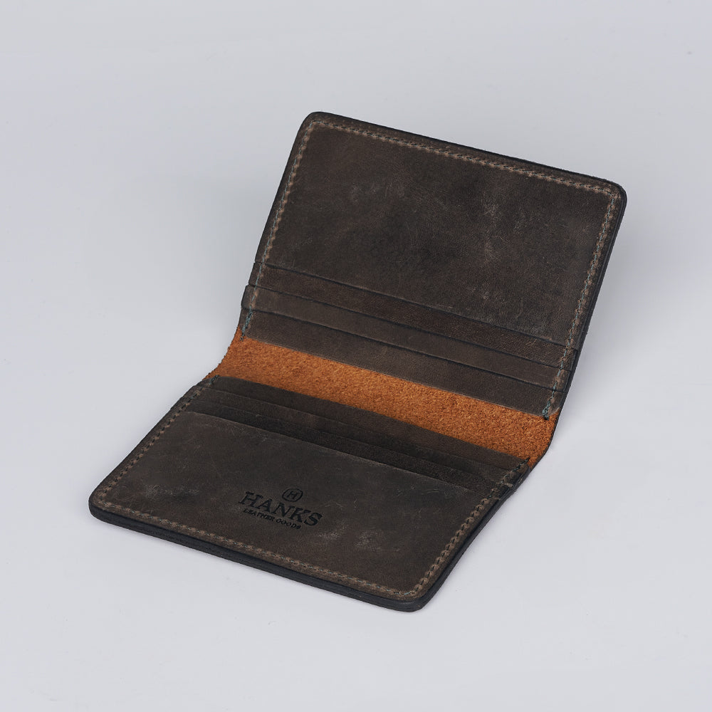 The Hanks Belts Diablo Slimline Card Holder, shown open on a white background, features dark brown bison leather, multiple card slots, and "HANKS" embossed inside. This slim card holder is made in the USA.