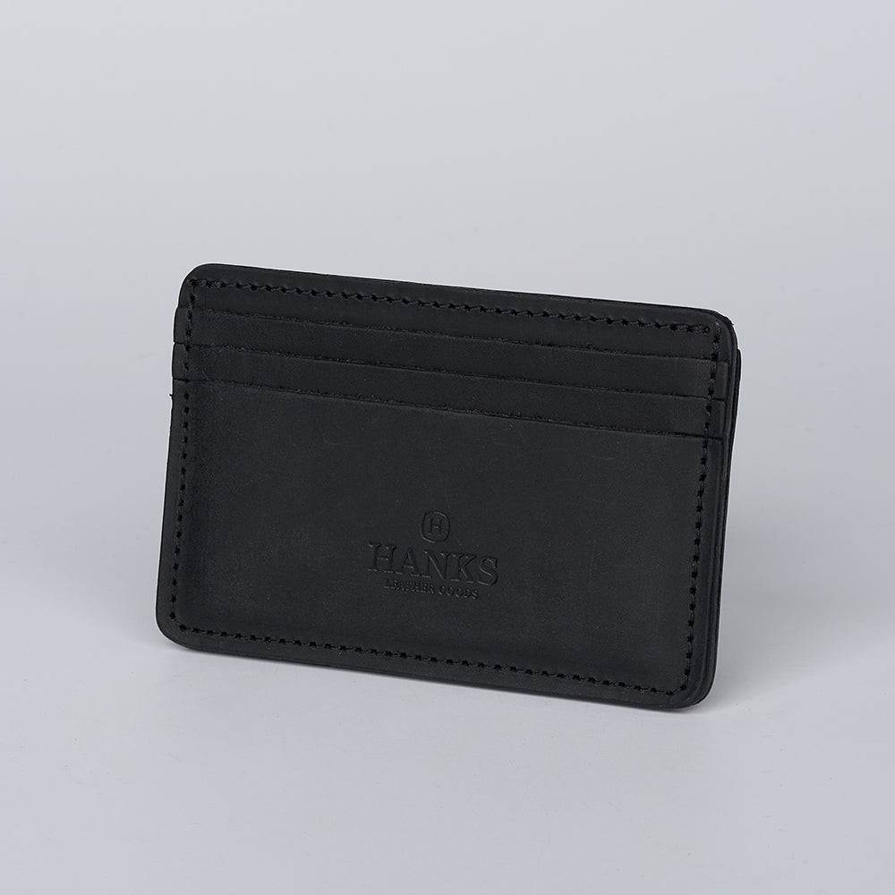 The Hamlin Card Holder with ID Window by Hanks Belts is crafted from black steerhide leather, features multiple slots, embossed "HANKS" and "USA," made in the USA, and shown on a plain light gray background.