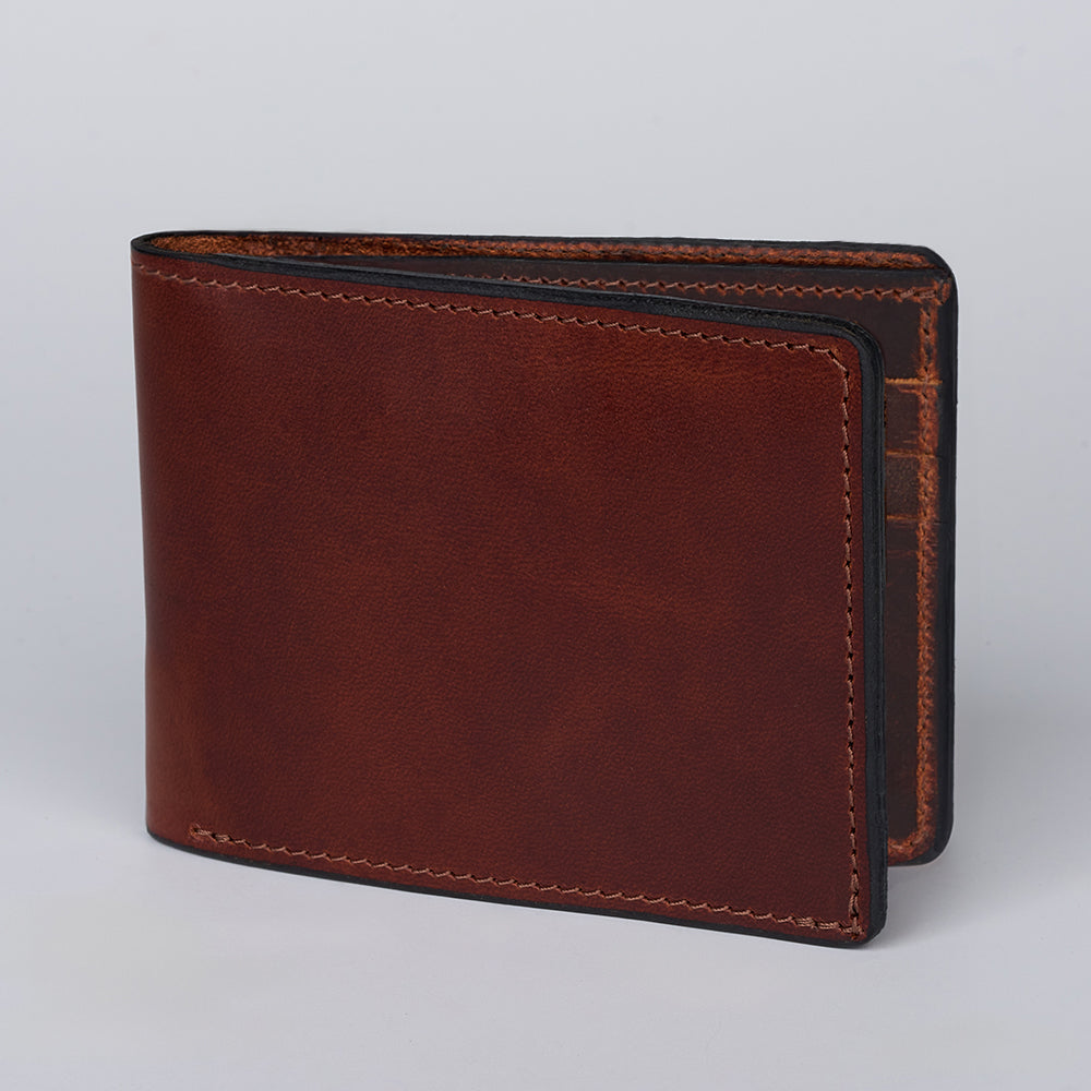 A Huron Premium Bifold with ID Window from Hanks Belts stands upright on a plain light gray background, highlighting its smooth steerhide leather texture, minimalist design, and visible edge stitching.