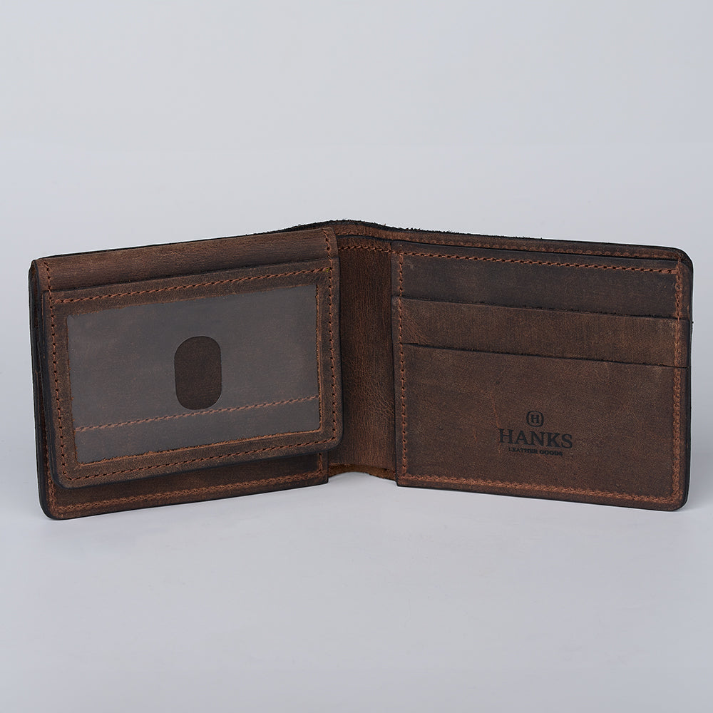 An open Huron Premium Bifold with ID Window by Hanks Belts, crafted from brown steerhide leather, features multiple card slots, a clear ID window, and "HANKS" stamping inside. Made in the USA, shown on a plain light background.
