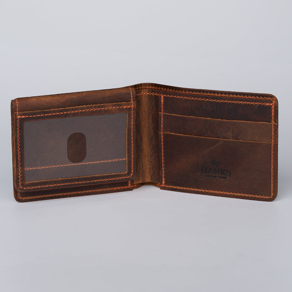 The Huron Premium Bifold with ID Window by Hanks Belts is an open brown steerhide wallet with orange stitching, card slots, and an ID window. "Hanks" is branded inside this USA-made wallet shown empty on a plain light background.