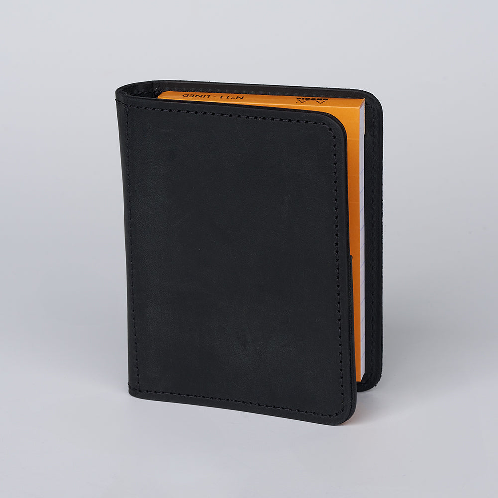 The Hanks Belts Notesman and Credit Card Wallet is a small black leather wallet with visible stitching, holding a yellow-edged notepad inside, shown upright against a plain light gray background.