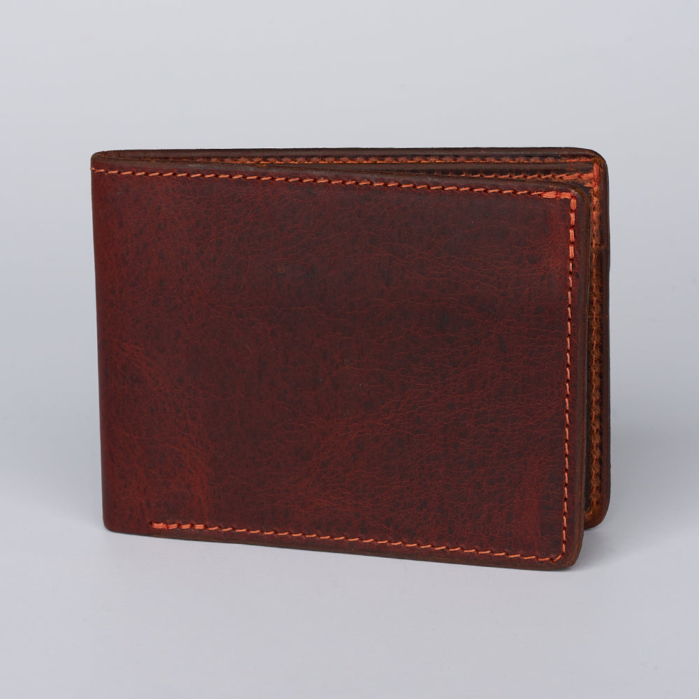 The Hanks Belts Ontario Premium Bison Bifold with ID Window, in brown leather with orange stitching, stands upright on a plain light gray background.