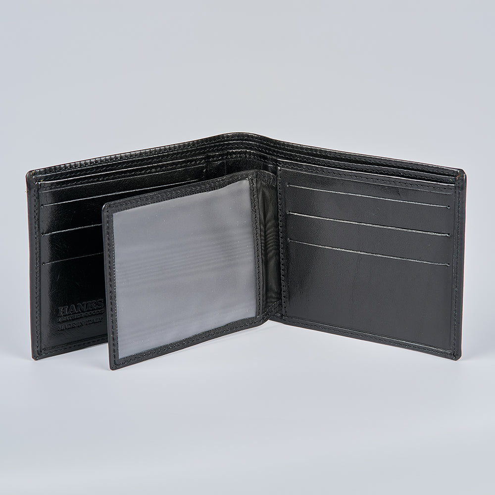 The Orta Italian Bifold with ID Window by Hanks Belts is open, revealing multiple card slots and a transparent flip-over ID compartment on the left, all in black handcrafted leather and shown empty.