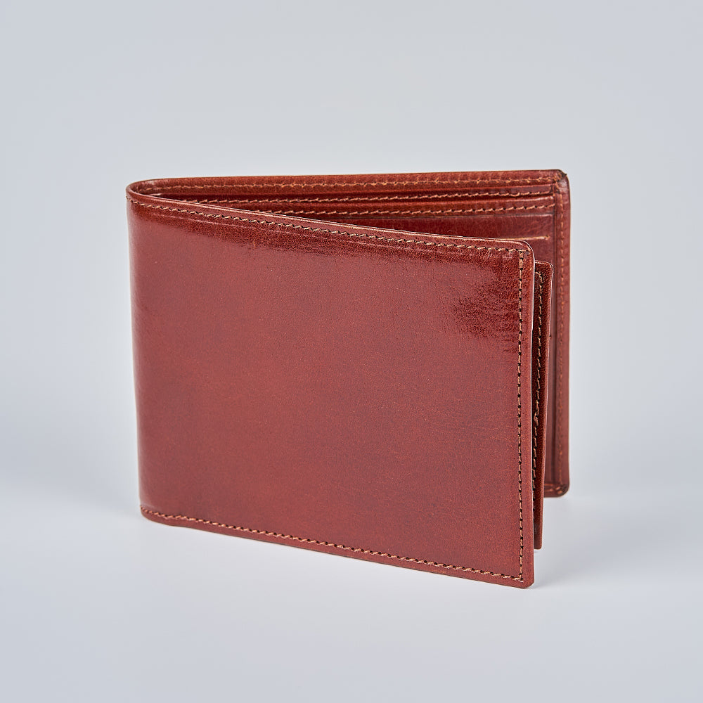 The Orta Italian Bifold with ID Window by Hanks Belts stands upright on a plain light gray background, highlighting its smooth leather texture and detailed edge stitching.