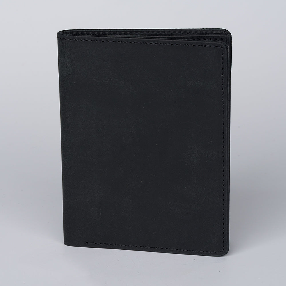 The Hanks Belts Passport Case Wallet, made from North American Steerhide leather, stands upright on a light gray surface with a plain black finish and no visible logos or decorations.