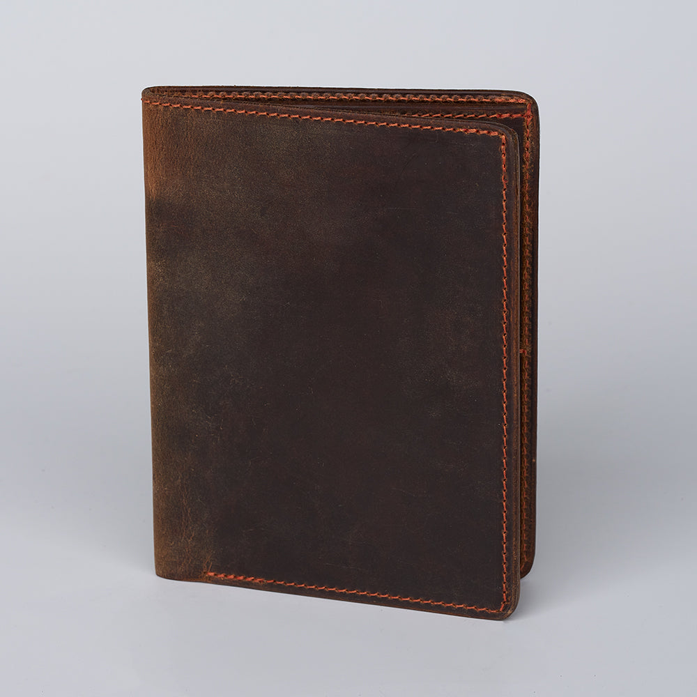 The Hanks Belts Passport Case Wallet, made from North American Steerhide leather with orange stitching, stands upright on a plain light gray background.
