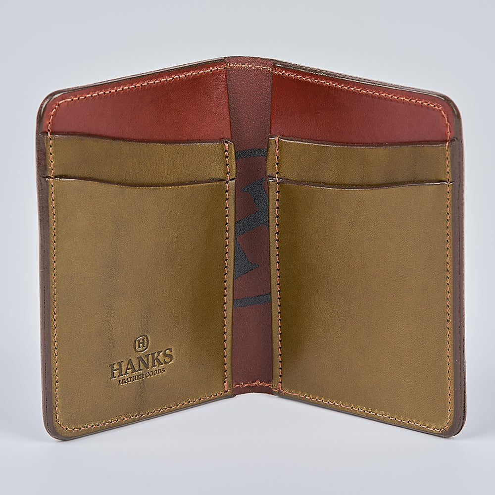 The Hanks Belts Superior Front Pocket Bifold is an open, handcrafted English Bridle Leather wallet with four interior card slots and the "HANKS" logo stamped on tan and reddish-brown panels. USA made and shown empty on a light gray background.