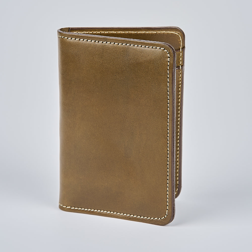 The Hanks Belts Superior Front Pocket Bifold stands upright on a light gray background, featuring white stitching and a smooth, polished brown English Bridle leather surface. Made in the USA, it showcases timeless style and quality craftsmanship.