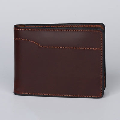 The Hanks Belts Tahoe Bifold, a closed brown steerhide leather wallet with visible stitching, stands upright against a plain light gray background.