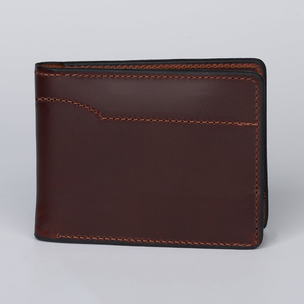 The Hanks Belts Tahoe Bifold, a closed brown steerhide leather wallet with visible stitching, stands upright against a plain light gray background.