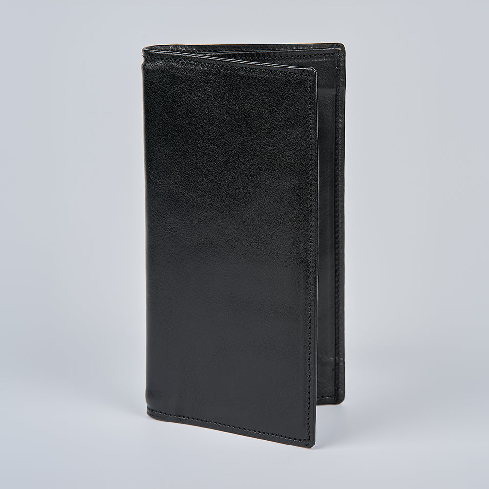 The Vico Italian Breast Pocket Bifold by Hanks Belts is a slim, black leather wallet standing upright on a light gray background. It’s closed, showcasing visible edge stitching and a smooth, glossy Italian leather finish.