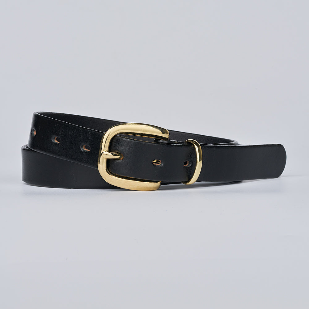 The Poppy by Hanks Belts is a black leather women’s statement belt with a brass buckle, elegantly coiled on a light gray background—an ideal accessory for any outfit.