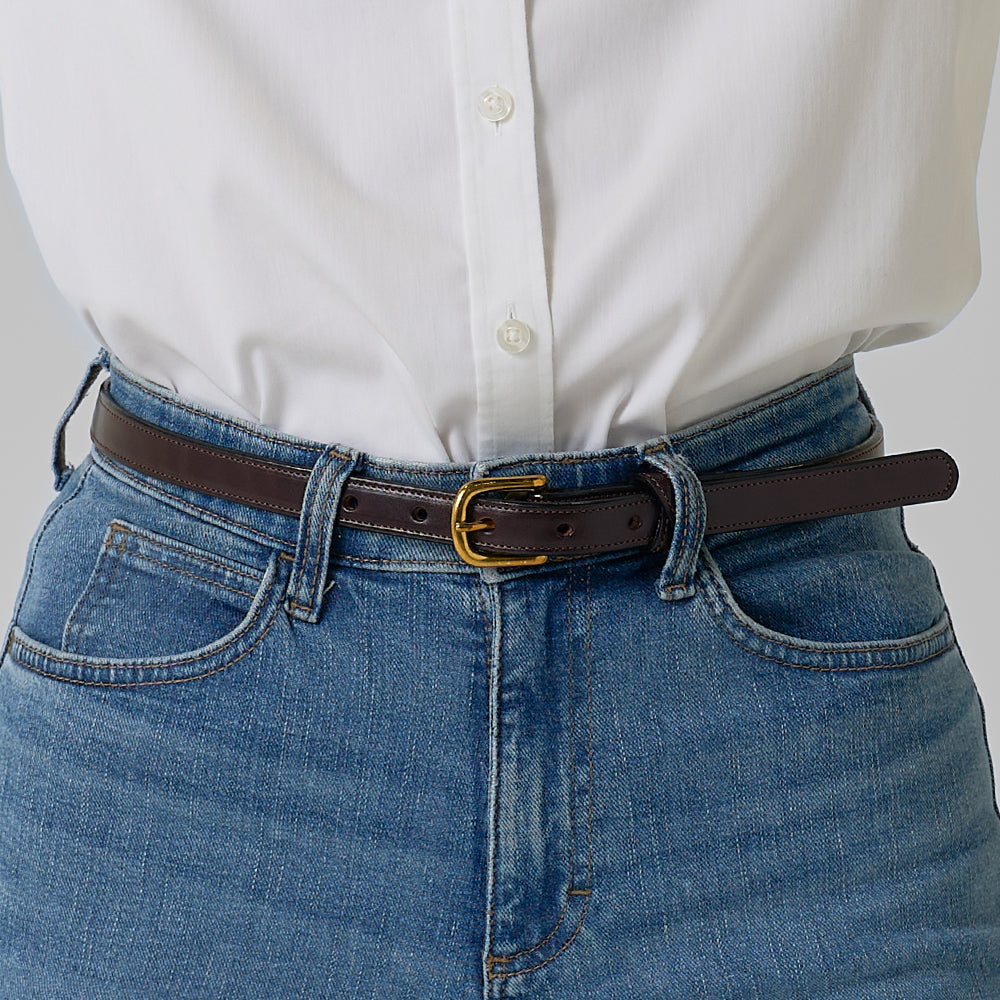 A person wears a white button-down shirt with blue jeans, accessorized with Hanks Belts’ The Dixie—a stylish women’s English Bridle leather belt featuring a dark brown strap and a gold buckle.