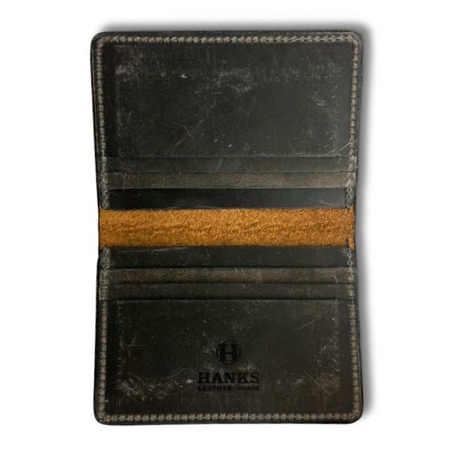 A slightly worn Diablo Slimline Card Holder by Hanks Belts is open, revealing two card slots and a horizontal brown suede strip in the middle. The logo "HANKS LEATHER USA" is embossed at the bottom center, below the card slots. This USA-made wallet shows some scuff marks and signs of use.