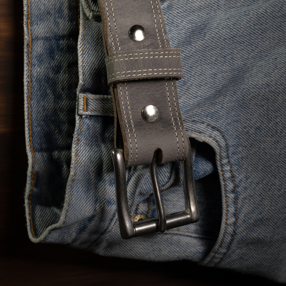 A close-up of light blue denim jeans with Hanks Belts' The Montana Bison Double Layer belt, featuring rugged bison leather, detailed stitching, and a stainless steel buckle threaded through the loops.