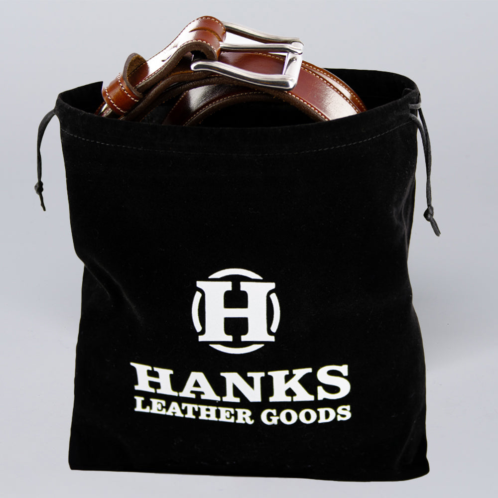 The Hanks Premium Velvet Gift Bag by Hanks Belts is a black drawstring bag with a bold "H" logo, perfect for storing belts; it holds two brown leather belts with metal buckles.