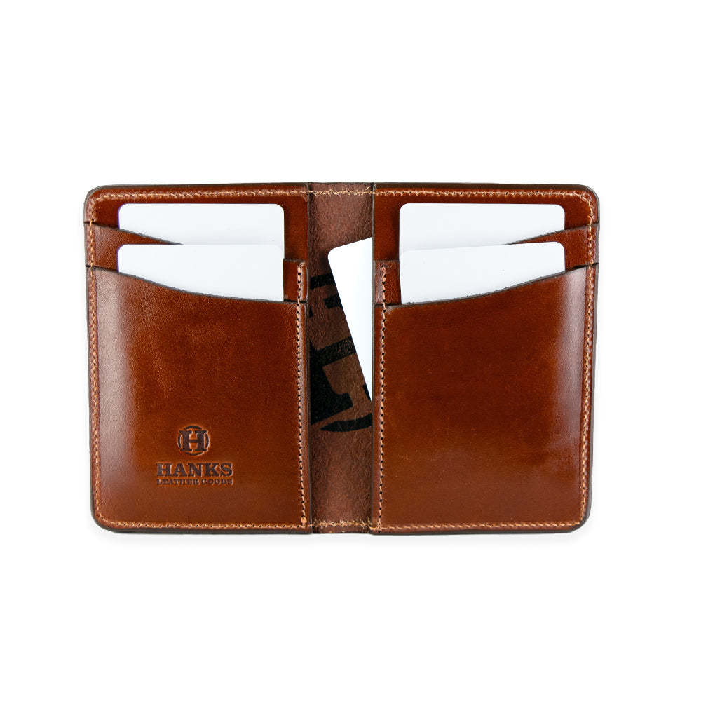 The Superior Front Pocket Bifold from Hanks Belts is an open brown handcrafted wallet with two sections, each holding three white cards. Made from USA-tanned leather, it features "HANKS" and a logo embossed on the bottom left corner.
