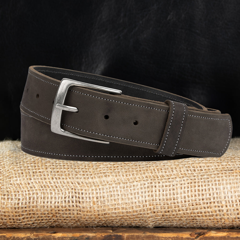 The Suede Belt - 1.5" by Hanks Belts, made in the USA, features a silver buckle, white-edged stitching, and adjustable holes. It rests on burlap with a dark background highlighting its texture and fine craftsmanship.