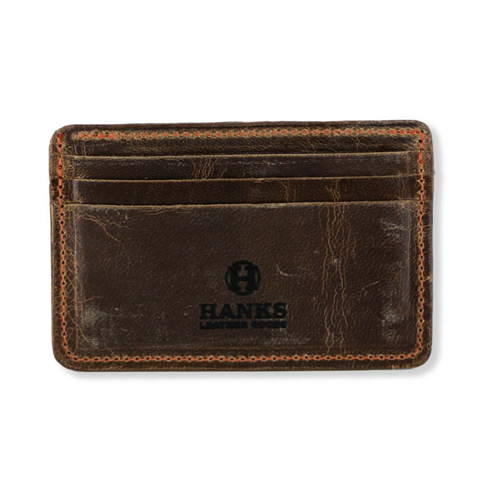 The Hamlin Card Holder with ID Window by Hanks Belts is a brown, worn-looking accessory made from durable Steerhide leather. It features three slots on the front and stitching around the edges. Proudly made in the USA, it showcases the "HANKS" logo in black at the bottom center.