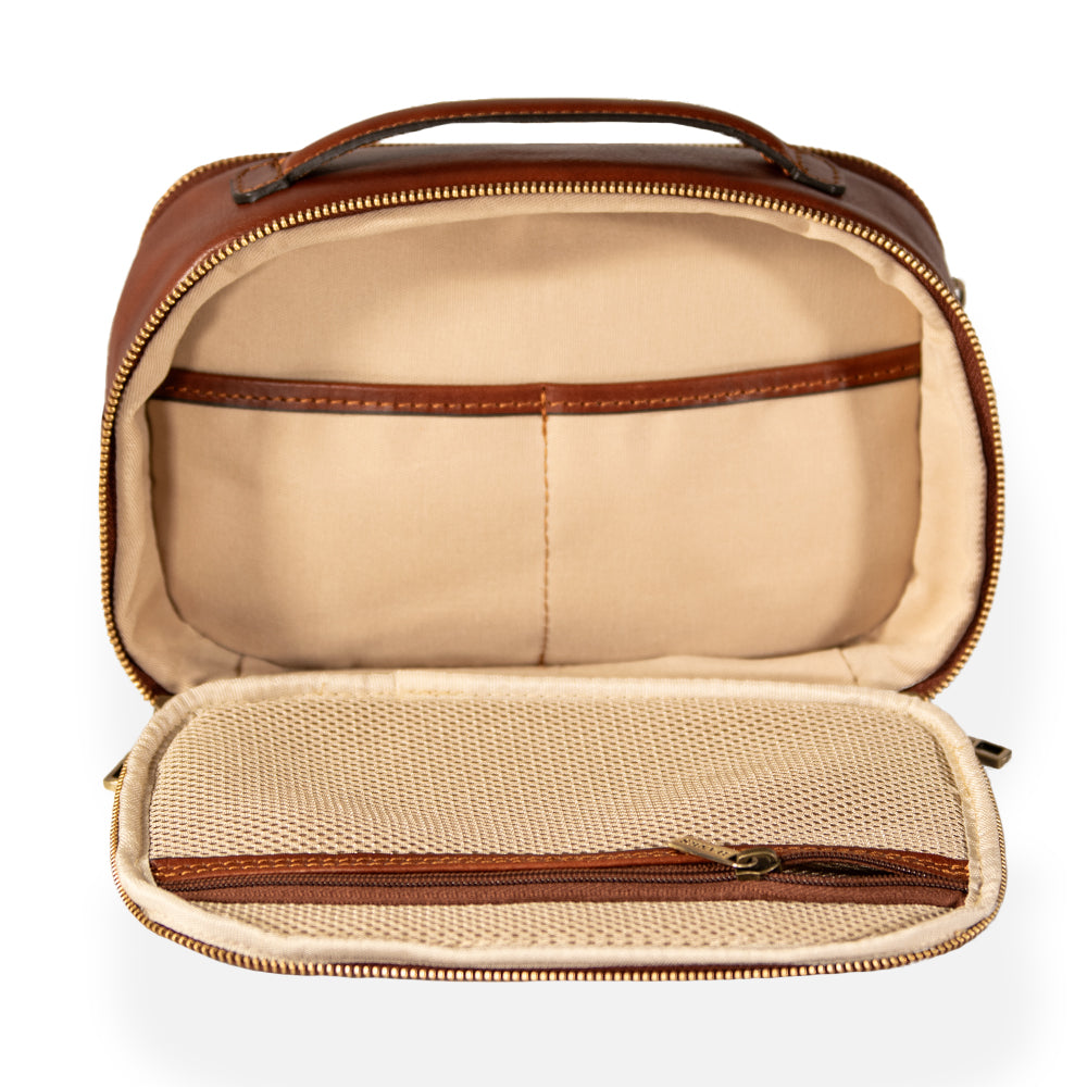 The Tidy Travel Case by Hanks Belts, exemplifying Italian craftsmanship, opens to reveal a cream-colored interior with two pockets. A mesh zipper pocket is neatly positioned on the flap. With a tan leather handle and a gold zipper, this luxurious travel case is both functional and elegant.
