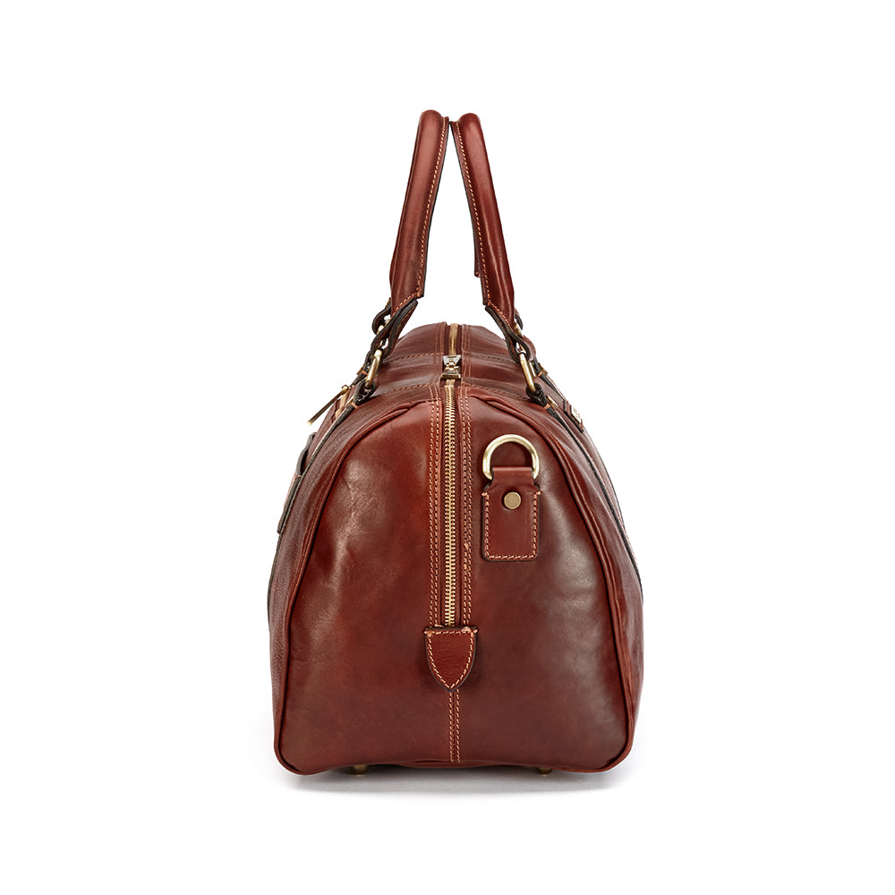 Witness the sophistication of the Hanks Belts' Getaway Duffel With Luggage Sleeve in this side view, crafted from luxurious Italian leather. It elegantly features two handles and a zipper, along with carry-on-friendly metal hardware details and a smooth texture, ideal for travelers who cherish elegance in every adventure.