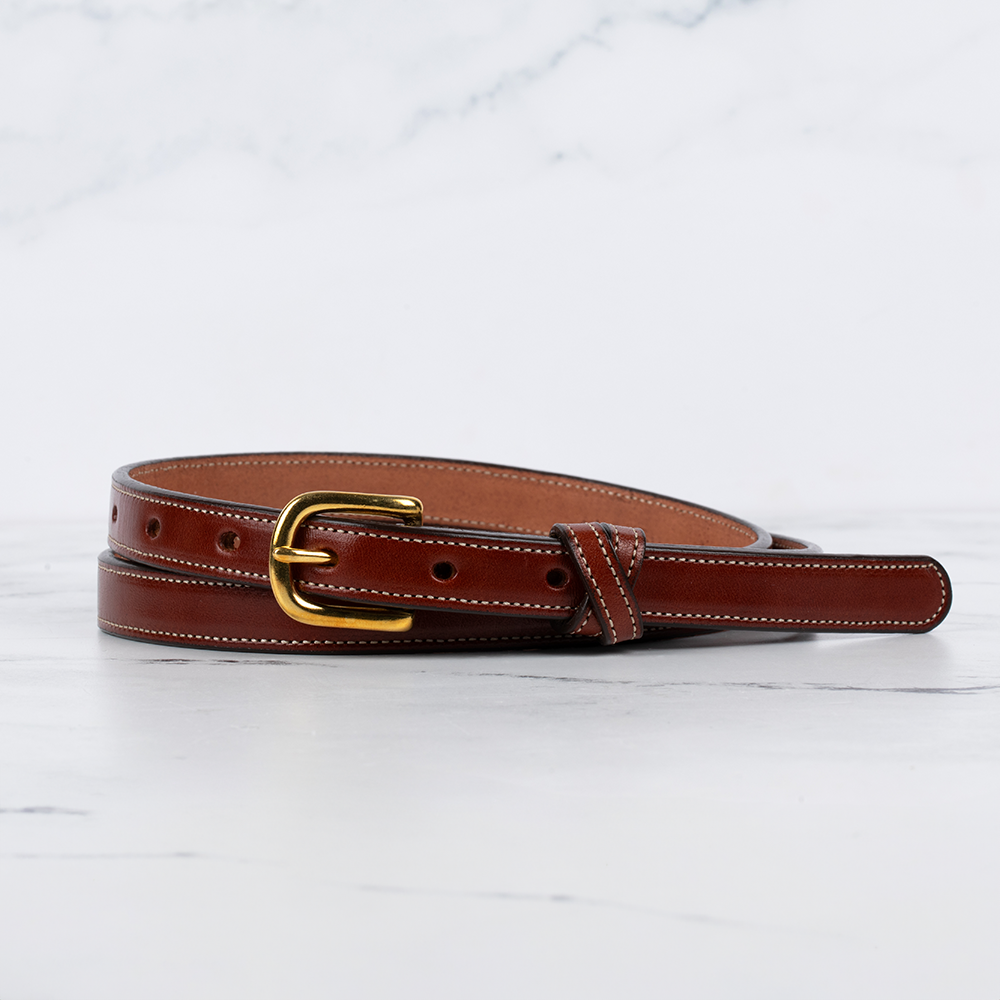 The Dixie by Hanks Belts is a women’s belt made from premium English Bridle leather, with white stitching and a gold buckle—artfully coiled on white marble to highlight its fine American craftsmanship.